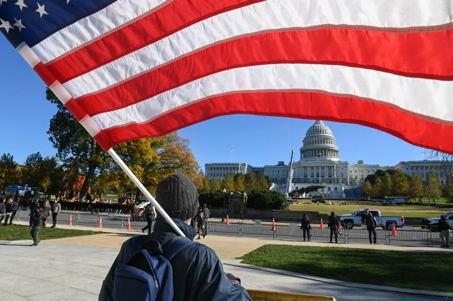 A man holds a US flag as he stands outside the West Lawn of the US Capitol building in Washington, DC on 19 November 2021. (Roberto Schmidt/AFP)