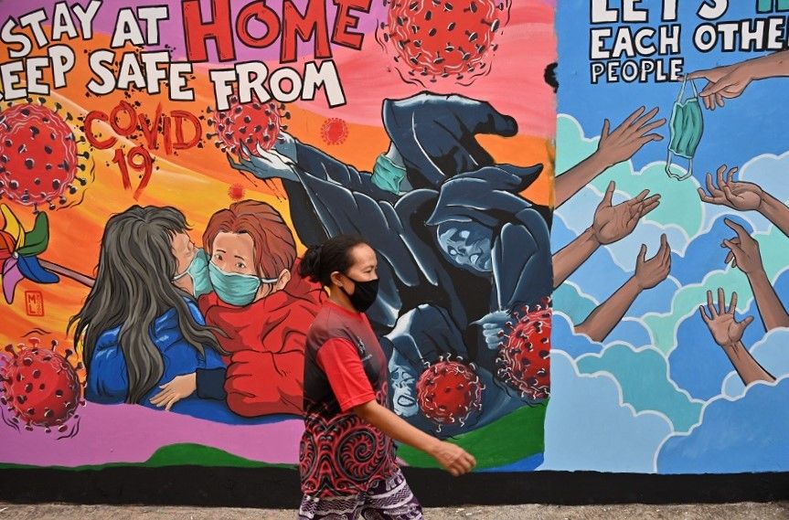 An Indonesian woman walks past a mural created by Indonesian artist Bayu Rahardian amid the Covid-19 coronavirus pandemic in Depok on 16 April 2020. (Adek Berry/AFP)