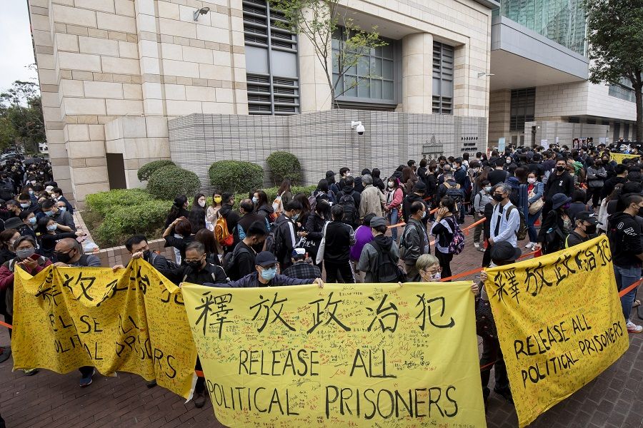 Pro-democracy demonstrators hold banners reading "Release all political prisoners" while waiting to enter the West Kowloon Magistrates' Courts ahead of a hearing for 47 opposition activists charged with violating the city's national security law in Hong Kong, China, on 1 March 2021. (Paul Yeung/Bloomberg)