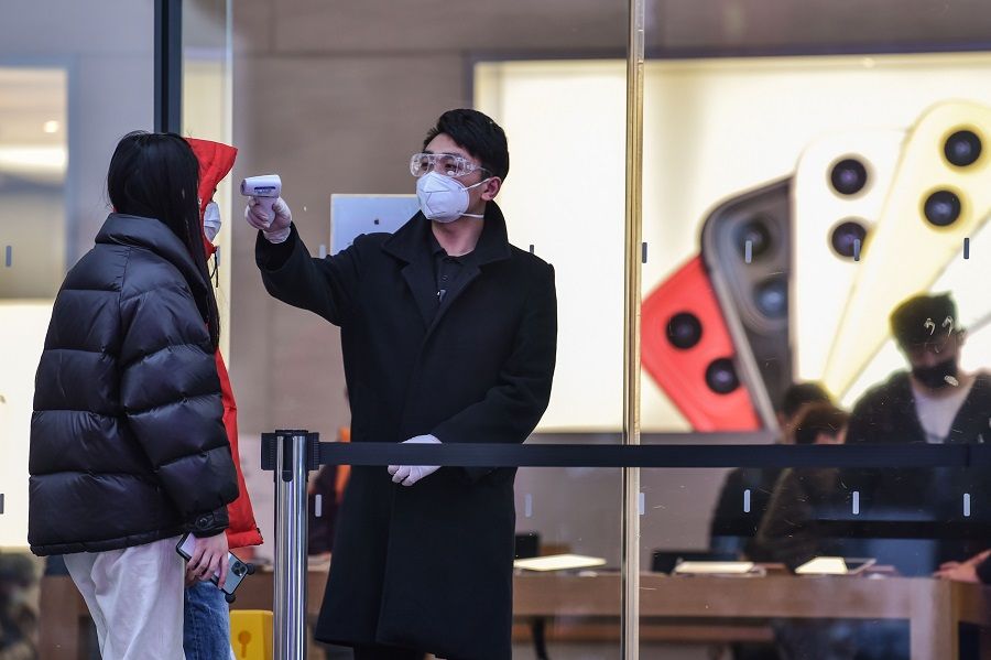 A security guard checks the temperature of customers at the entrance of an Apple store in Shanghai on 28 February 2020. (Hector Retamal/AFP)