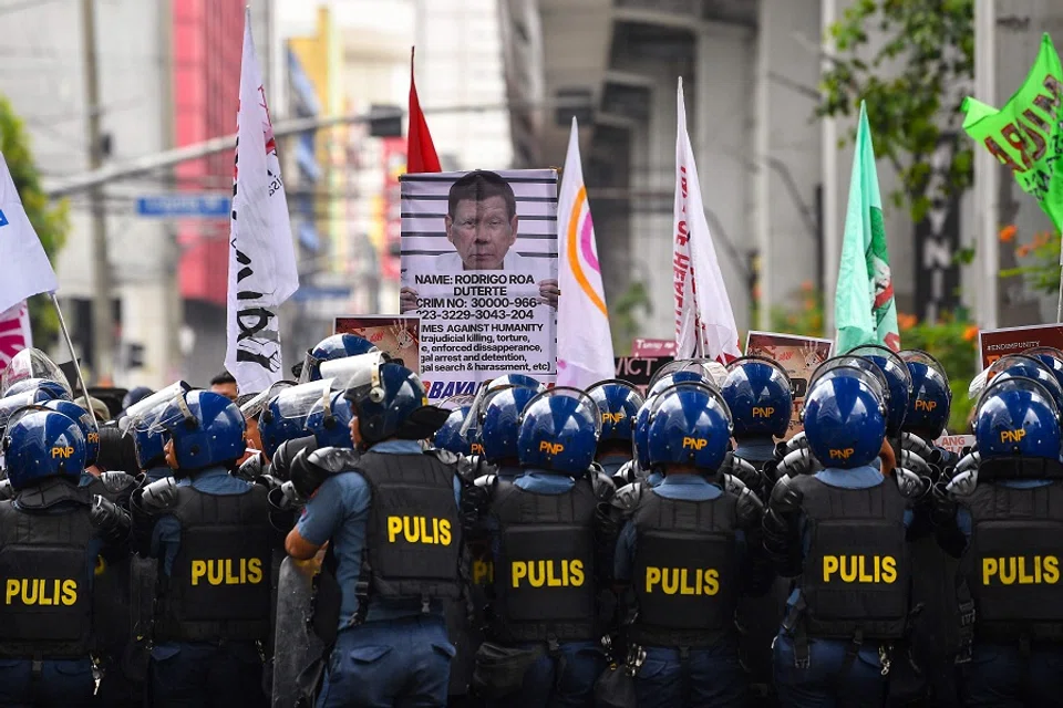 Protesters carrying a placard showing former president Rodrigo Duterte are blocked by anti-riot policemen near Malacanang palace in Manila on 17 March 2025. (Ted Aljibe/AFP)