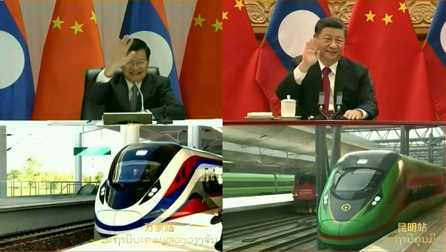 This file frame grab from Lao National TV video footage taken on 3 December 2021 via AFPTV shows Laos President Thongloun Sisoulith (top left) and China's President Xi Jinping (top right) waving as they watch trains connecting the Chinese city of Kunming (pictured bottom right) and the Laos capital Vientiane (pictured bottom left) set off during the opening of a Chinese-built railway which took five years to construct under China's trillion-dollar Belt and Road Initiative. (Lao National TV via AFPTV/AFP)