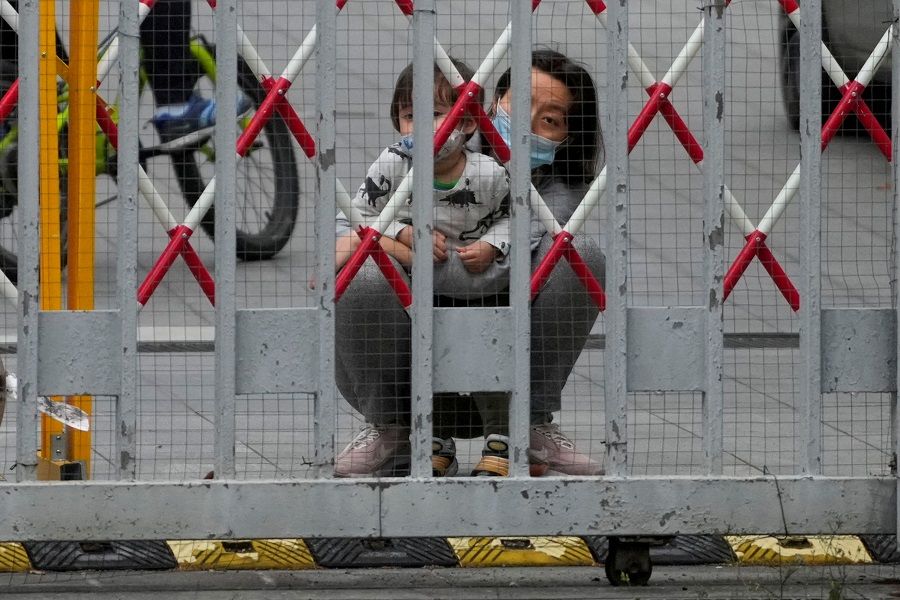 A resident and a child look out through gaps in the barriers at a closed residential area during lockdown, amid the Covid-19 pandemic, in Shanghai, China, 10 May 2022. (Aly Song/Reuters)