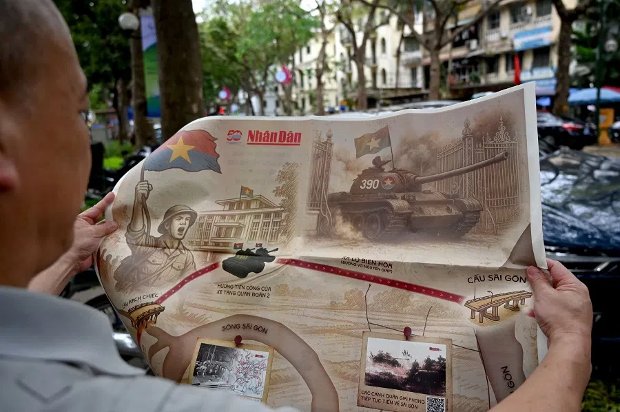 A man reads the Nhan Dan newspaper in Hanoi on 25 April 2025, featuring an illustration of Tank 390 crashing through the gates of Saigon’s presidential palace on 30 April 1975. (Nhac Nguyen/AFP)
