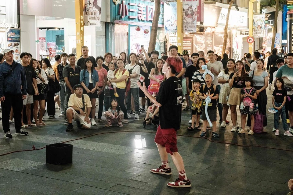 People watch a street performer on a street in Taipei on 26 May 2024. (Yasuyoshi Chiba/AFP)