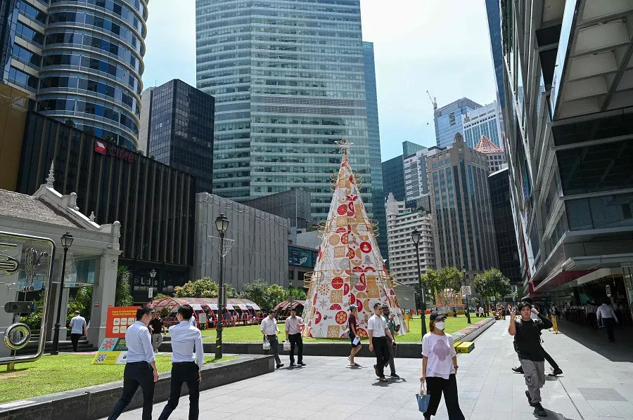 People walk past a decorative Christmas tree on display at the Raffles Place financial district in Singapore on 5 December 2023. (Roslan Rahman/AFP)