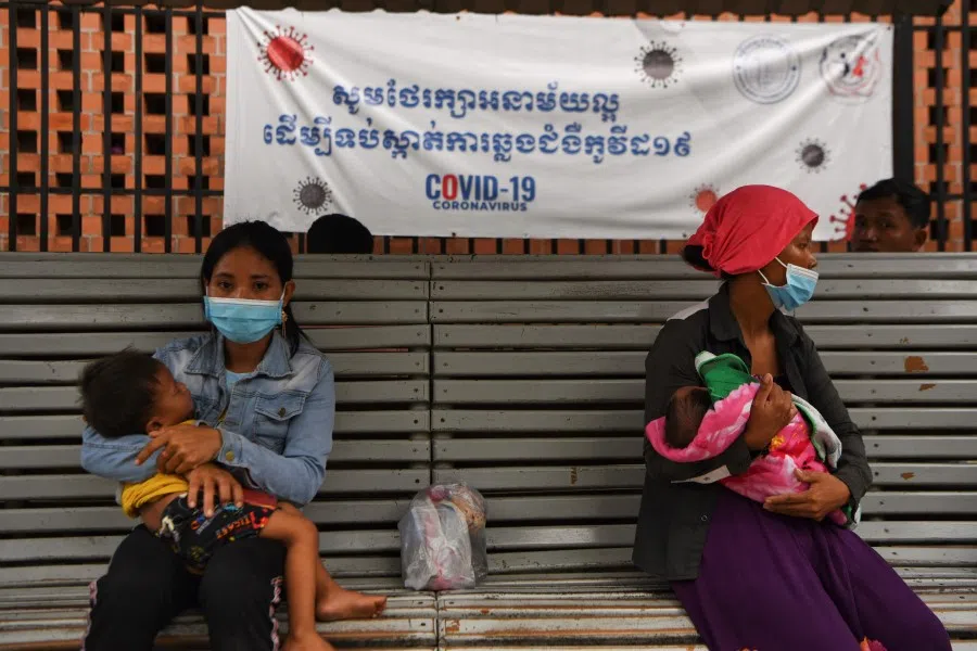 Women wearing face masks amid concerns over the spread of the Covid-19 coronavirus, carry their child outside a hospital with a banner warning about the virus in Phnom Penh on 29 September 2020. (Tang Chhin Sothy/AFP)