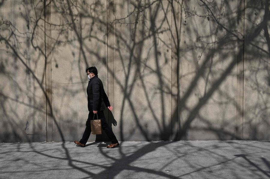 A man wearing a face mask walks along a road in Beijing on 11 March 2020. (Wang Zhao/AFP)