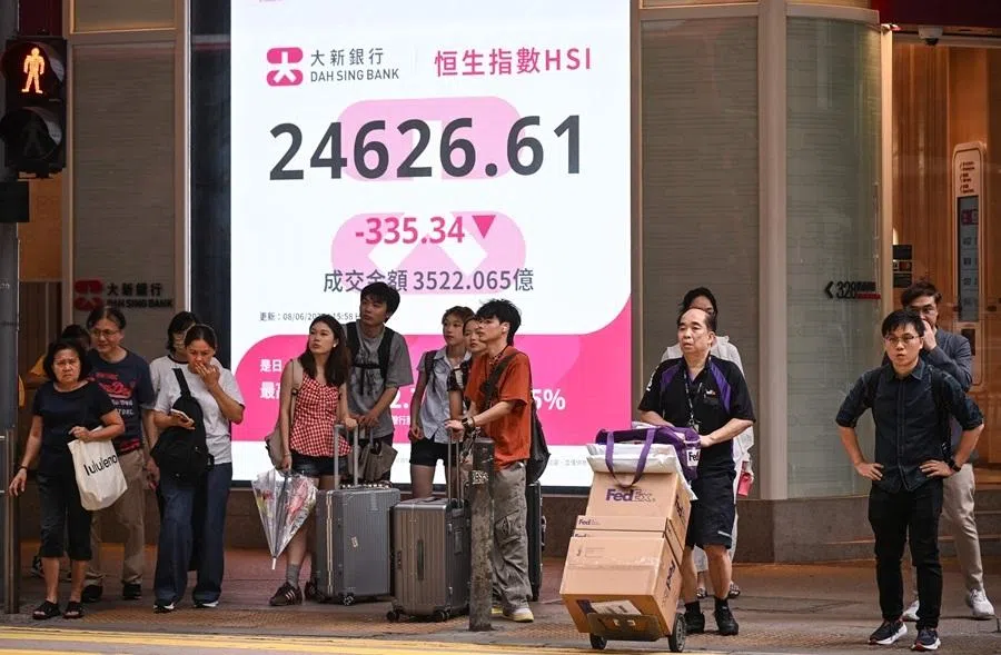 Pedestrians wait to cross a street in front of an electronic sign board showing the Hang Seng Index in Hong Kong on 8 June 2026.
