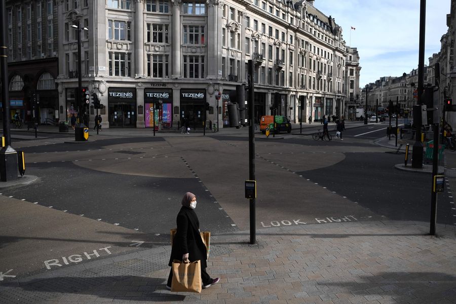 A woman wearing a protective face mask walks through a quiet Oxford Circus in central London on the afternoon of 21 March 2020 (Daniel Leal-Olivas/AFP)