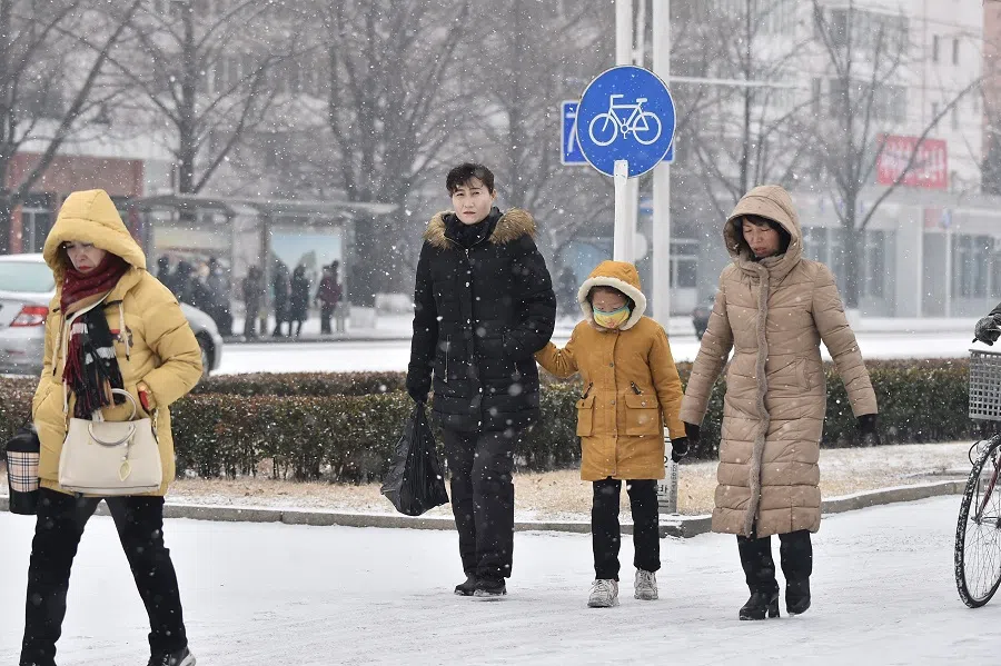 People walk on a street of Pothong Gate as it snows in Pyongyang on 13 January 2025. (Kim Won Jin/AFP)