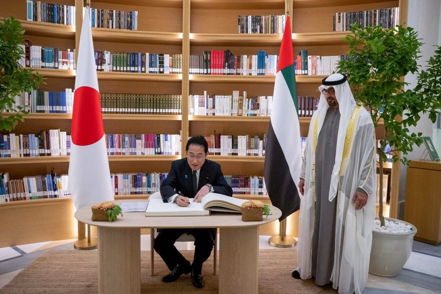 This handout image provided by the UAE Ministry Of Presidential Affairs shows UAE President Sheikh Mohamed bin Zayed al-Nahyan (R) standing by as Japan's Prime Minister Fumio Kishida signs the guest book during an official reception at Qasr al-Watan in Abu Dhabi on 17 July 2023. (Hamad Al-Kaabi/UAE's Ministry of Presidential Affairs/AFP)