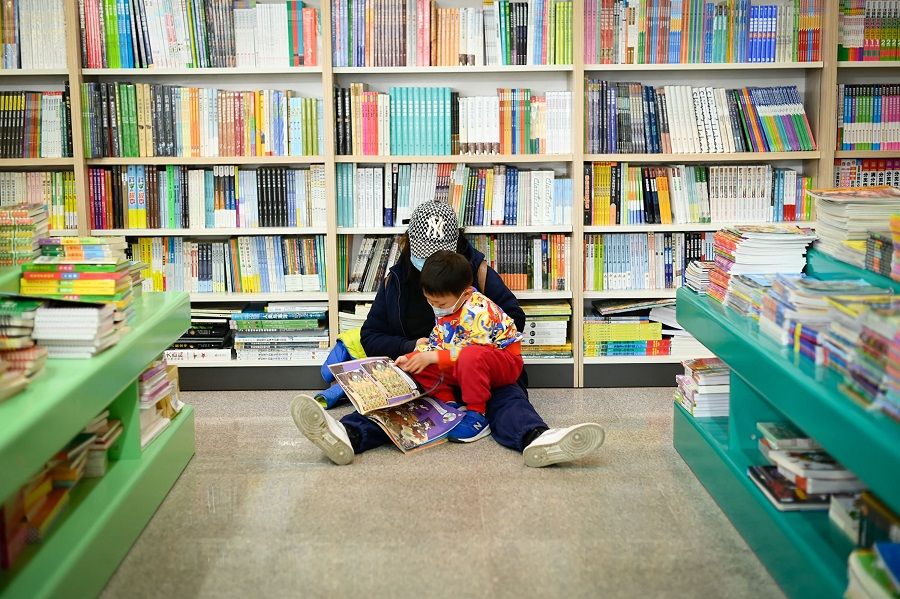 A child reads while sitting on a guardian's lap at a bookstore in Beijing, China, on 6 April 2022. (Wang Zhao/AFP)