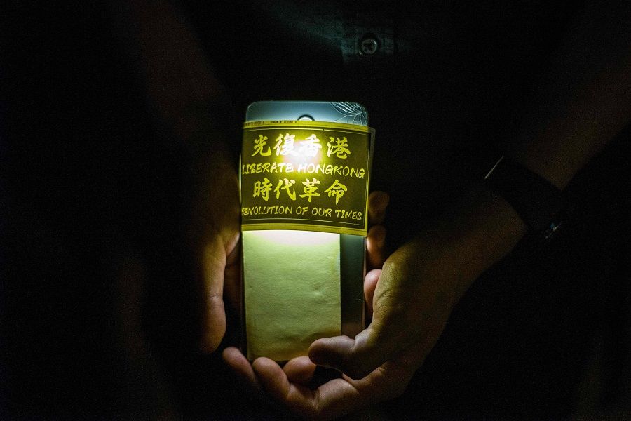 A pro-democracy activist holds his phone while queueing to pay respects to mark the one year anniversary of a man who fell to his death after hanging a protest banner against the now-withdrawn extradition bill on the scaffolding outside a shopping mall, in Hong Kong on 15 June 2020. (Anthony Wallace/AFP)