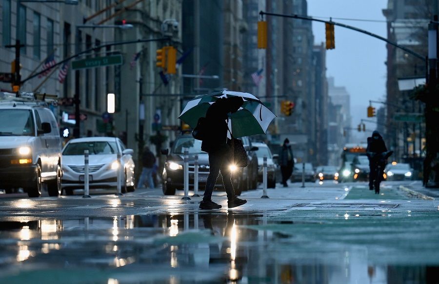A person holding an umbrella crosses a street after heavy rainfall on 30 November 2020 in New York City. (Angela Weiss/AFP)