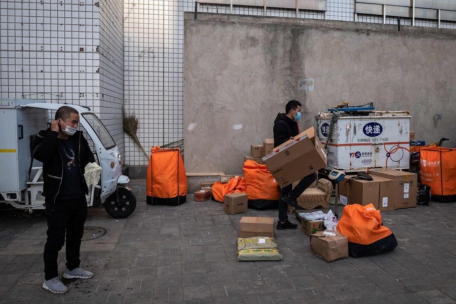Delivery workers wearing face masks amid concerns over the Covid-19 coronavirus sort out their delivery items on a street in Beijing on 22 April 2020. Restrictions on travel and the flow of goods across borders could have adverse impacts on BRI projects. (Nicolas Asfouri/AFP)