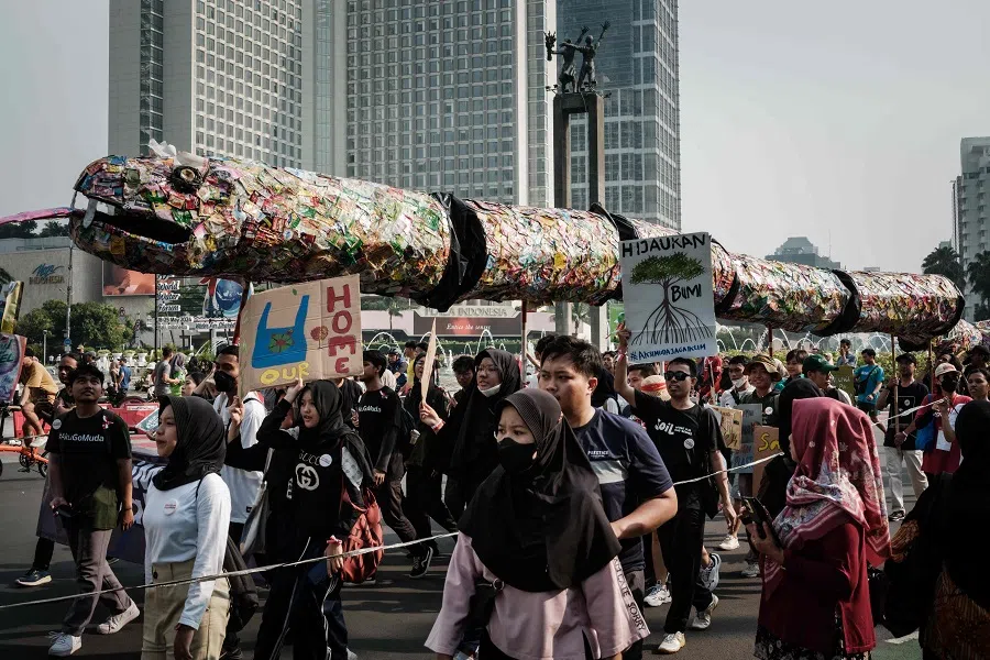 Youths hold placards and carry a snake-shaped object made of plastic waste druing their protest against the climate change on the street during a car-free day in Jakarta on 5 May 2024.