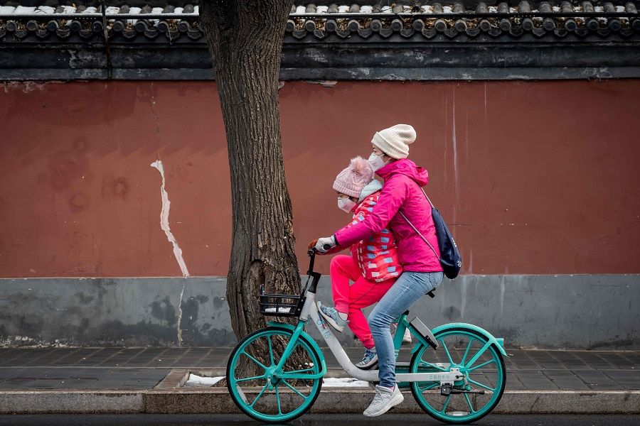 A woman and a girl wearing protective masks to prevent the spread of Covid-19 ride on a bicycle in Beijing on 2 February 2020. (Nicolas Asfouri/AFP)
