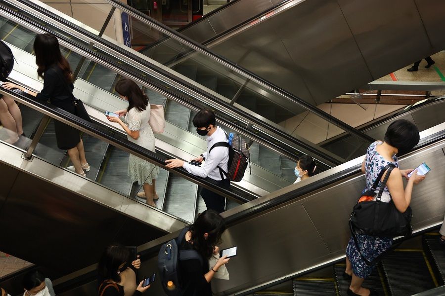 People looking at their mobile phones while taking the escalators at Raffles Place MRT station in Singapore on 3 January 2022. (SPH Media)