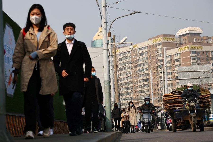 People wearing face masks walk along a street in Beijing, following outbreaks of the coronavirus disease (Covid-19) in China, 25 October 2021. (Thomas Peter/Reuters)