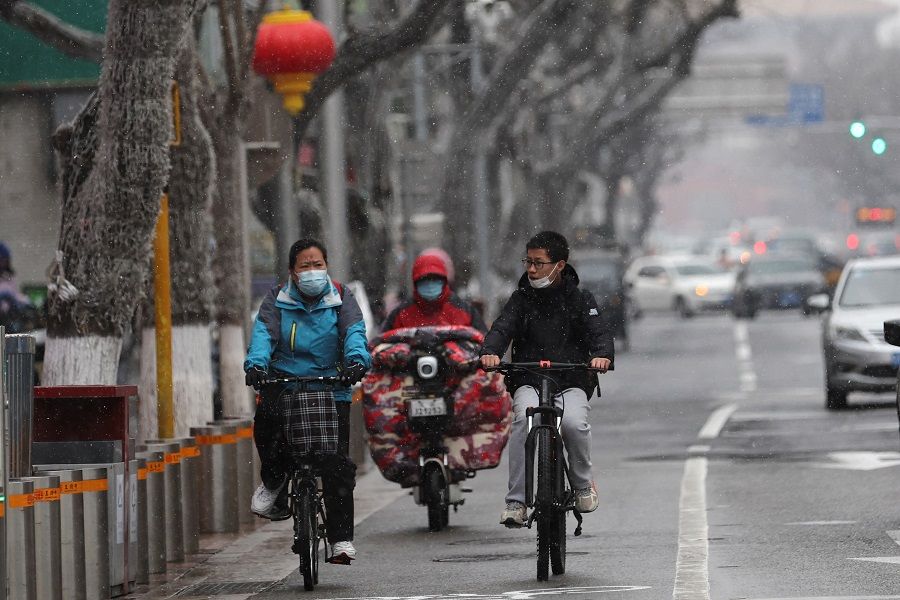 People ride bikes on a street amid snowfall, in Beijing, China, 17 March 2022. (Tingshu Wang/Reuters)