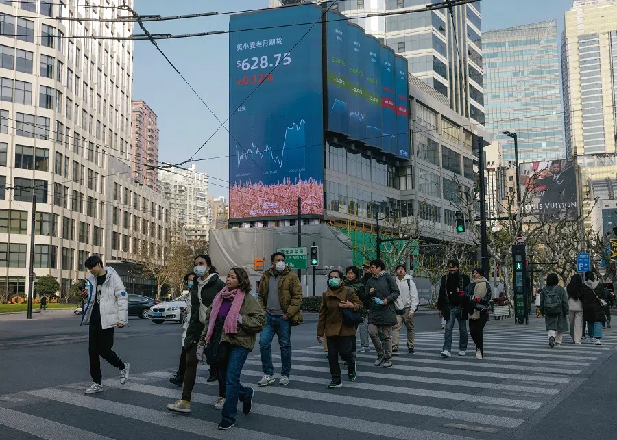 People cross the street beneath a large screen showing the latest stock exchange and economy data in Shanghai, China, on 2 January 2024. (EPA-EFE/Alex Plavevski)