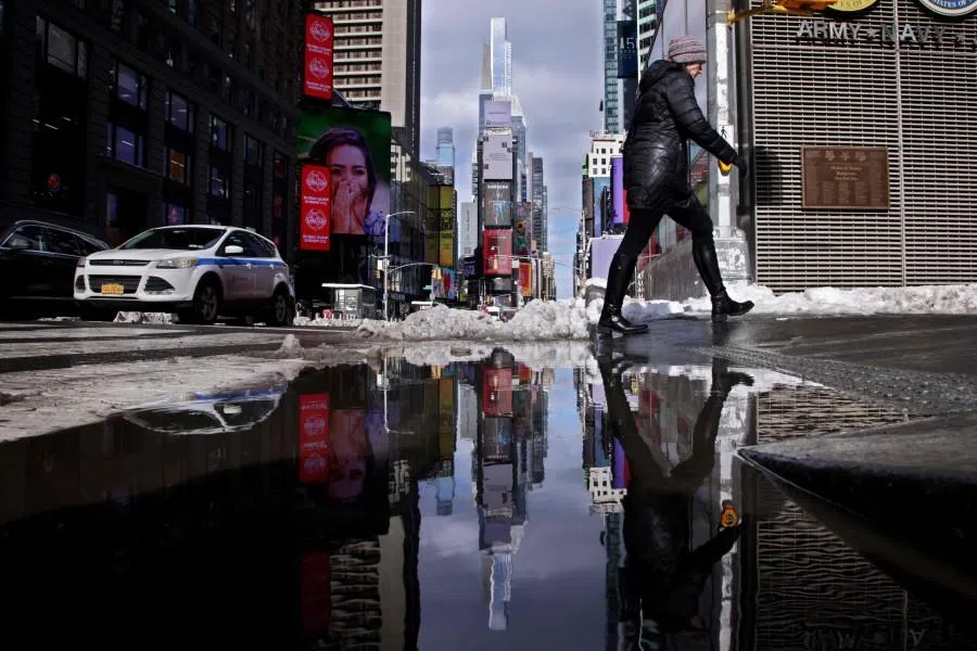People walking on the street are reflected in melted snow the day after a winter storm in New York on 24 February 2026.