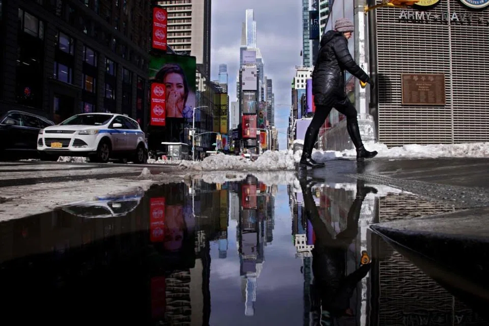People walking on the street are reflected in melted snow the day after a winter storm in New York on 24 February 2026. (Leonardo Munoz/AFP)