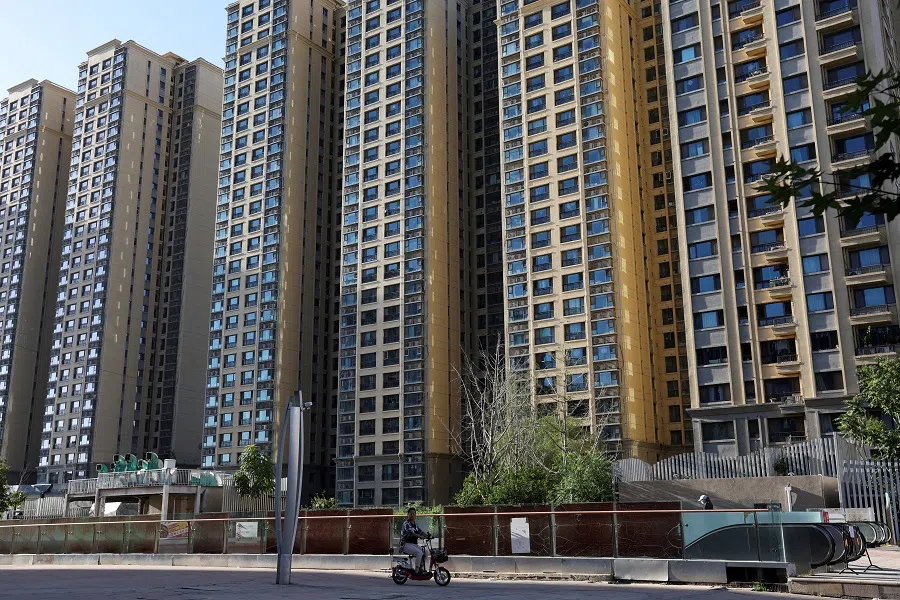A woman rides a scooter past residential buildings at a residential complex in Beijing, China, on 27 September 2023. (Florence Lo/Reuters)