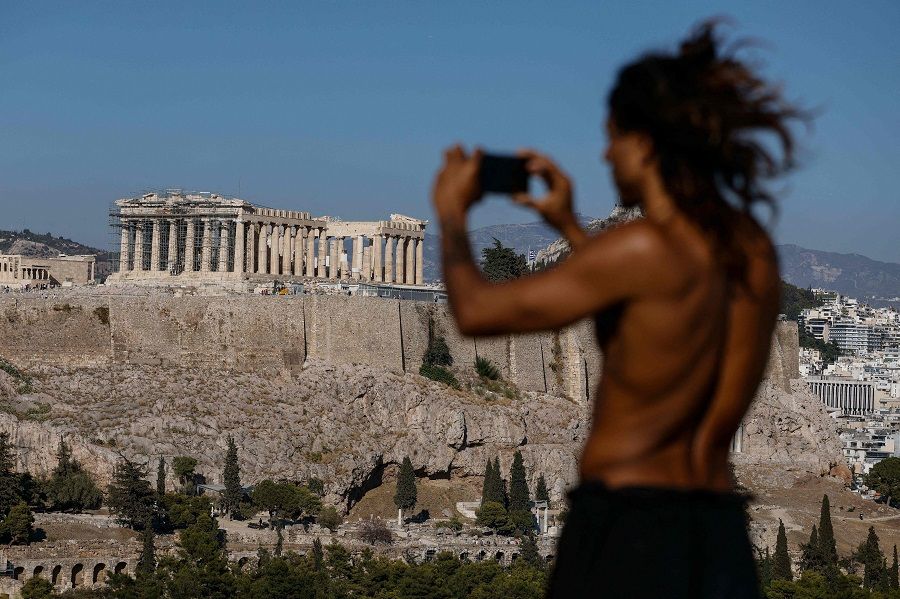 A man takes a photo from a hill overlooking the Ancient Acropolis archeological site in Athens, Greece on 5 October 2021. (David Gannon/AFP)