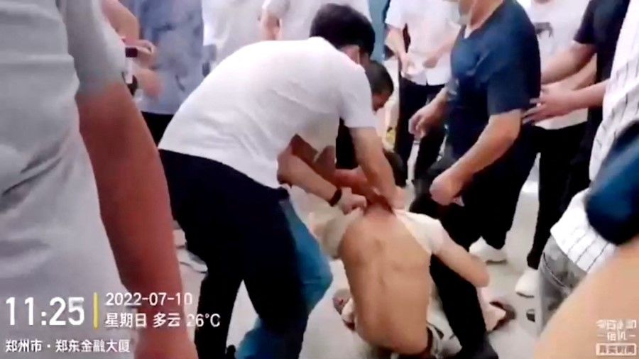 Plain-clothed security personnel pull on a demonstrator's shirt while dragging him away during a protest over the freezing of deposits by some rural-based banks, outside a People's Bank of China building in Zhengzhou, Henan province, China, 10 July 2022, in this screengrab from video obtained by Reuters. (Reuters)