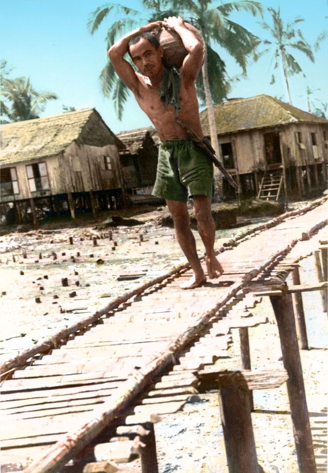 A worker carries a vat of water at a kelong in Singapore, 1950s. Seaside kelongs had no water supply and wells had to be dug, both for daily use as well as for the fishing boats.
