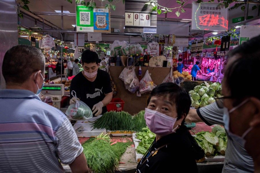 This file photo taken on 20 June 2020 shows a vendor (2nd L) selling vegetables at his stall at a market in Beijing. (Nicolas Asfouri/AFP)