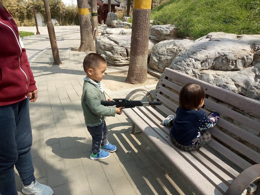 A two-year-old boy pointing a toy rifle at my son, wanting to play with him.