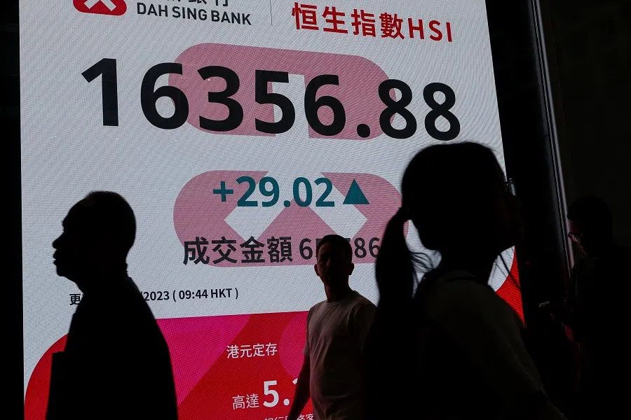 People walk past a screen displaying the Hang Seng Index in Central district, Hong Kong, China, on 6 December 2023. (Tyrone Siu/Reuters)