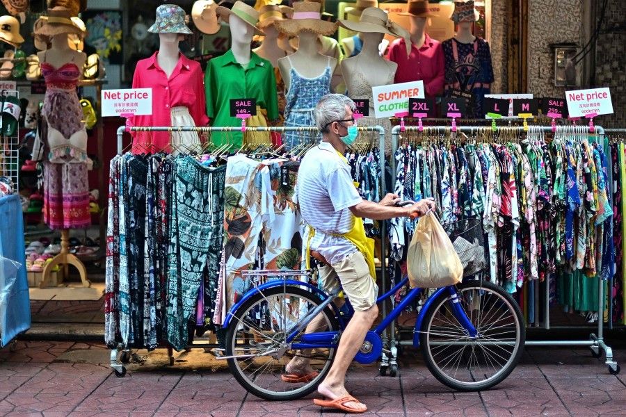 A man on a bicycle is seen in front of clothes for sale in the Chinatown area of Bangkok on 9 June 2023. (Manan Vatsyayana/AFP)