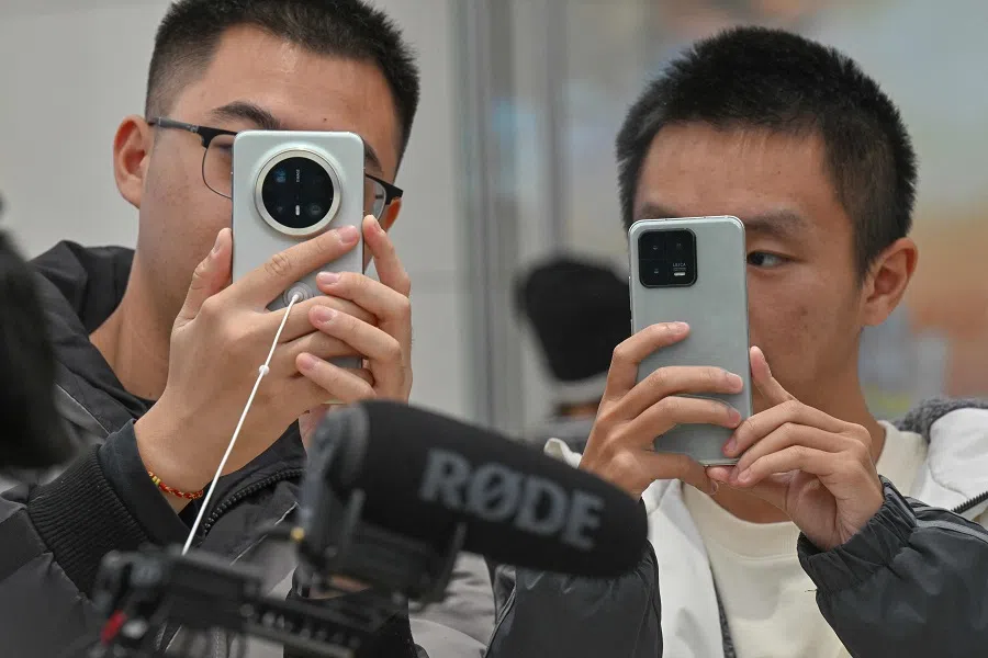 People look at mobile phones at the Wangfujing shopping area in Beijing on 26 November 2024. (Adek Berry/AFP)