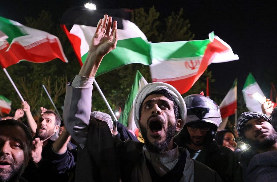 Demonstrators wave Iran's flag and Palestinian flags as they gather in front of the British embassy in Tehran, Iran, on 14 April 2024, after Iran launched a drone and missile attack on Israel. (Atta Kenare/AFP)