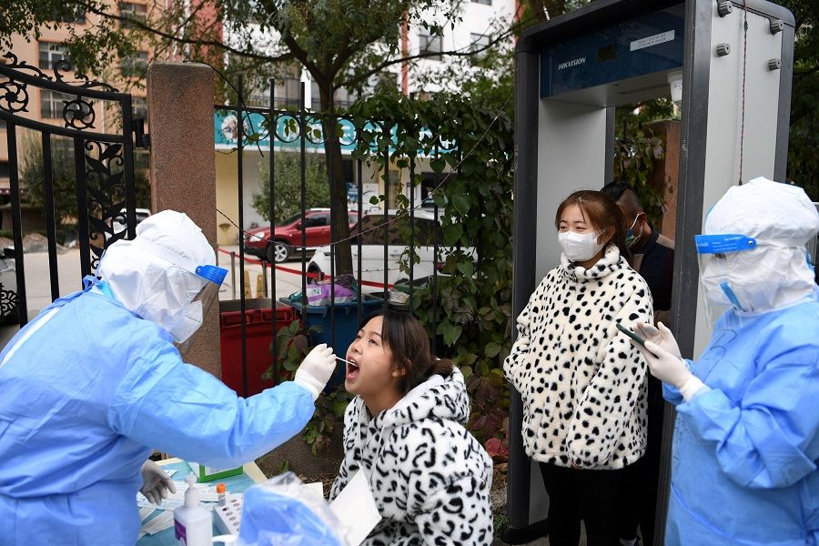 A medical worker in protective suit collects a swab from a resident at a free nucleic acid testing site following new Covid-19 cases in Lanzhou's Chengguan district, Gansu province, China, 20 October 2021. (CNS photo via Reuters)