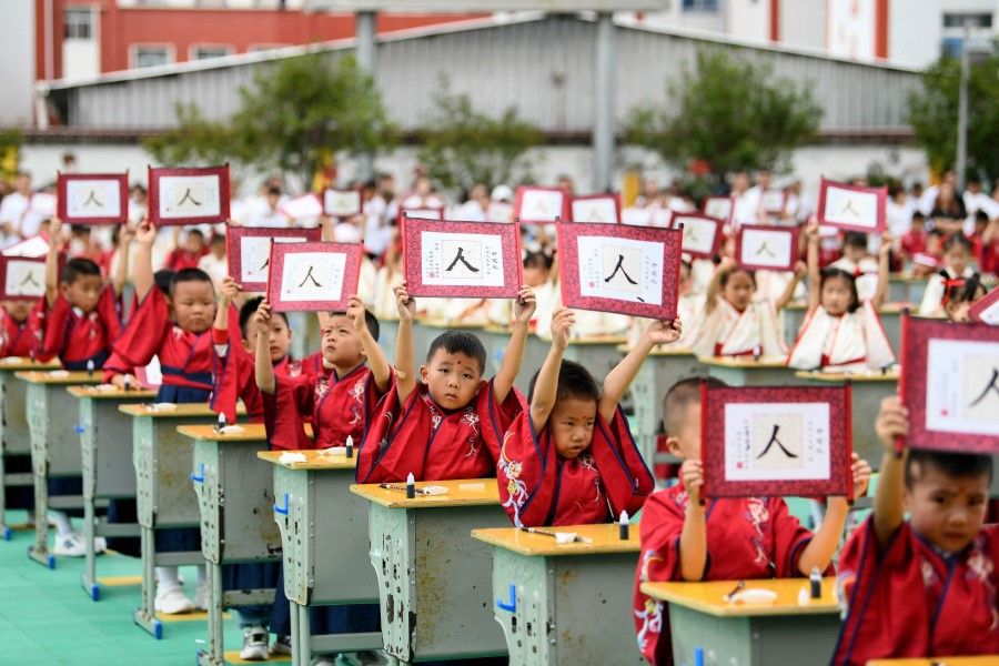 First-grade students wearing Hanfu clothing hold up cards with the character "ren" meaning "person" during an initiation ceremony to learn about traditional culture at a primary school in Anlong County, in China's southwest Guizhou province, on 28 August 2023. (AFP)