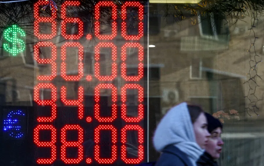 Pedestrians walk past an electronic board showing currency exchange rates of the US dollar and euro against the Russian rouble in a street in Moscow, Russia, on 20 March 2025. (Evgenia Novozhenina/Reuters)