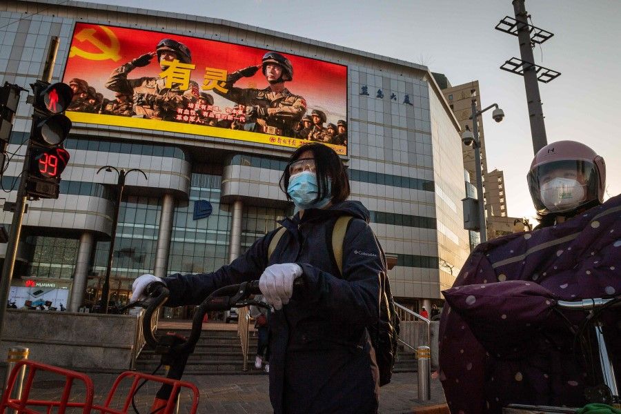 People wait at a traffic light in front of a giant screen displaying a propaganda image (top) on a street in Beijing, 20 April 2020. (Nicolas Asfouri/AFP)