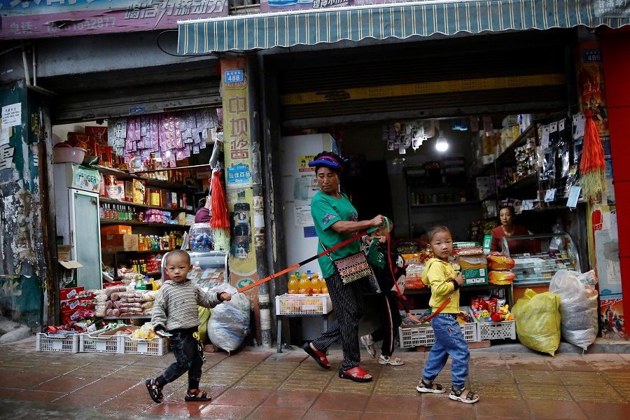 An ethnic Yi woman holds anti-lost straps tied on children's wrists as they walk past shops in Ganluo county, Liangshan Yi Autonomous Prefecture, Sichuan province, China, 10 September 2020. (Tingshu Wang/Reuters)