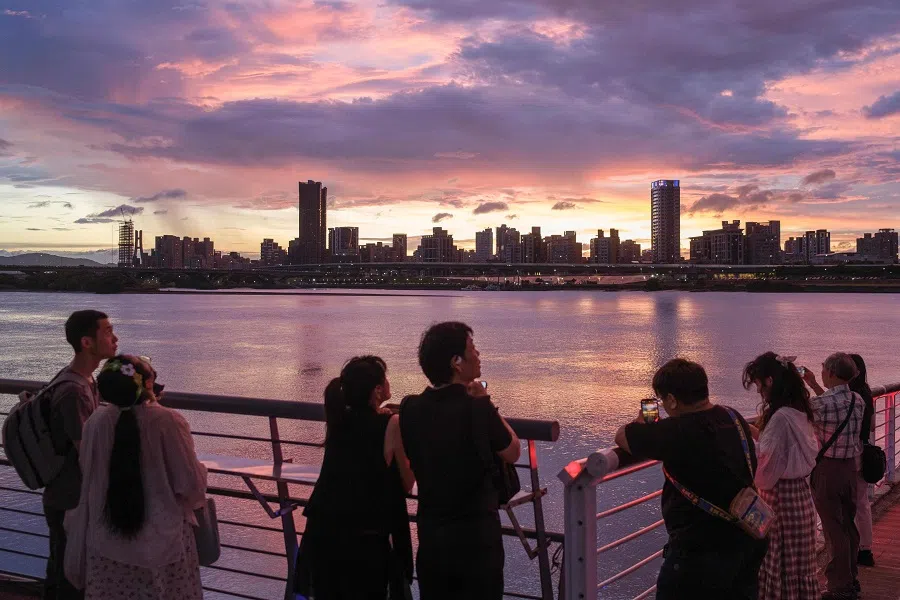 People take pictures of Taipei’s skyline along the bank of Tamsui River during sunset from the Dadaocheng Wharf popular tourist spot in Taipei on 16 September 2024. (Yan Zhao/AFP)