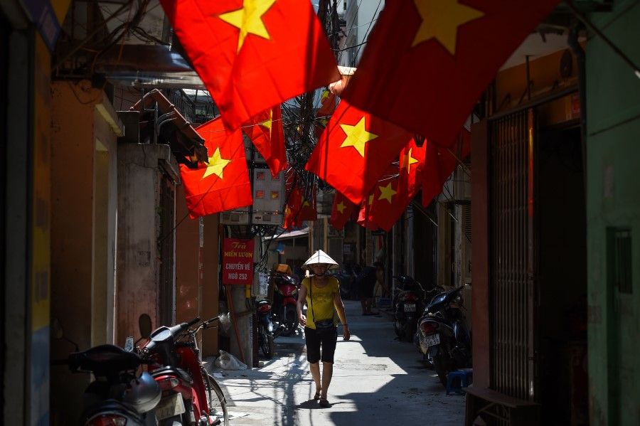A woman walks along along an alleyway decorated with Vietnamese national flags in Hanoi, 1 September 2020. (Nhac Nguyen/AFP)