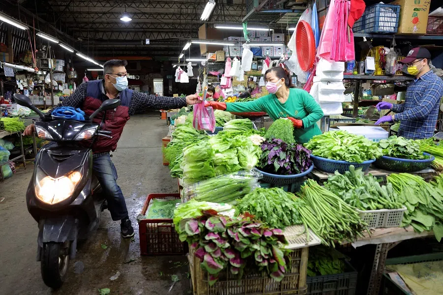 A rider wearing a face mask to prevent the spread of Covid-19 hands a bag to a vegetable vendor at a market in Taipei, Taiwan, 22 April 2022. (Annabelle Chih/Reuters)