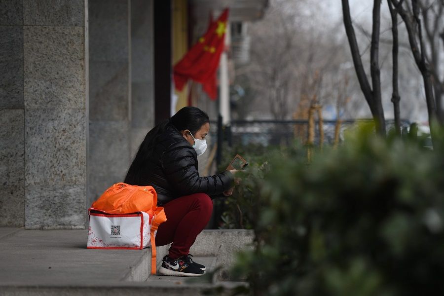 A woman wears a face mask as a preventive measure against the Covid-19 coronavirus as she looks at her mobile phone near the entrance of the Peking University People's Hospital in Beijing on 21 February 2020. (Greg Baker/AFP)