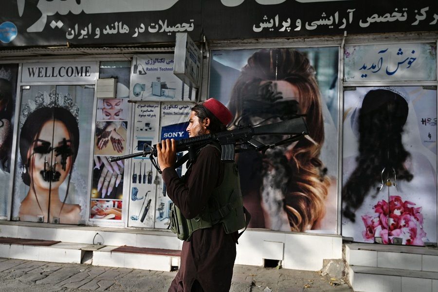 A Taliban fighter walks past a beauty salon with images of women defaced using spray paint in Shahr-e Naw in Kabul, Afghanistan, on 18 August 2021. (Wakil Kohsar/AFP)