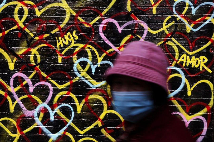 A woman wearing a protective face mask walks by a graffiti painted wall in the Chinatown neighborhood of New York City, US, 11 May 2023. (Shannon Stapleton/Reuters)