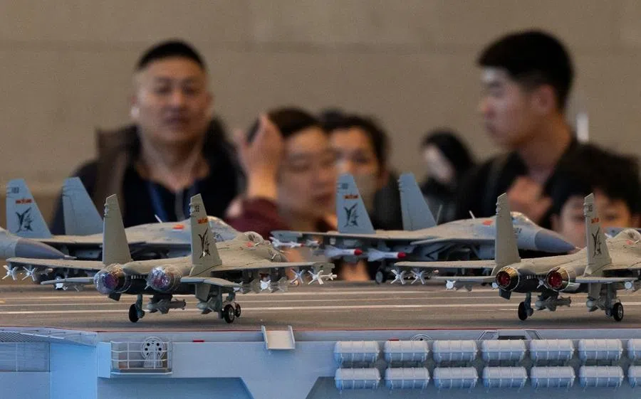 People gather around a model of an aircraft carrier with jet fighters positioned on its upper deck, at an exhibition on China’s manufacturing achievements, at the National Museum in Beijing, China, on 24 March 2026.